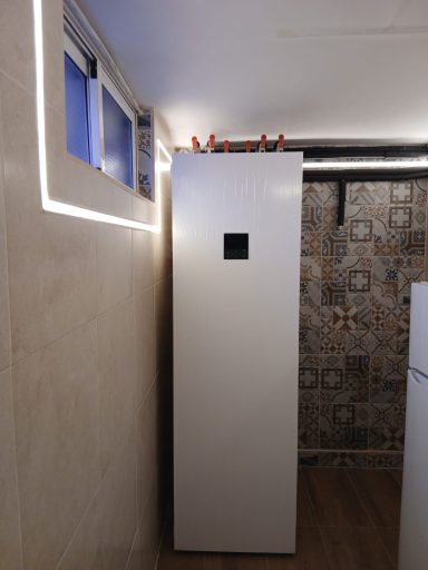 Ud. interior compacta aerotermia Un frigorífico blanco colocado en un rincón con una ventana al fondo.
